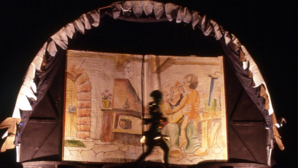 Talking Cricket in front of the book of Pinocchio by the Compagnia dei Folli