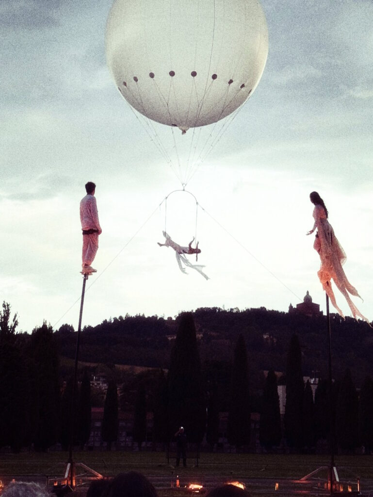 artists on sway poles watching a female artist on the hot air balloon during sunset