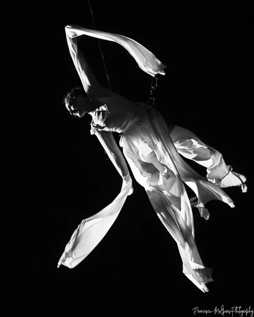 aerialist suspended in the air with white silks