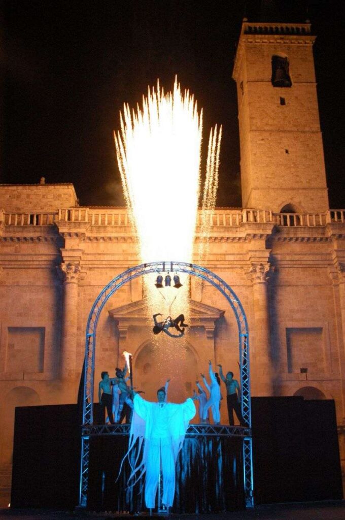 Angelo sui trampoli della Compagnia dei Folli con fuochi d'artificio dietro, Inferno